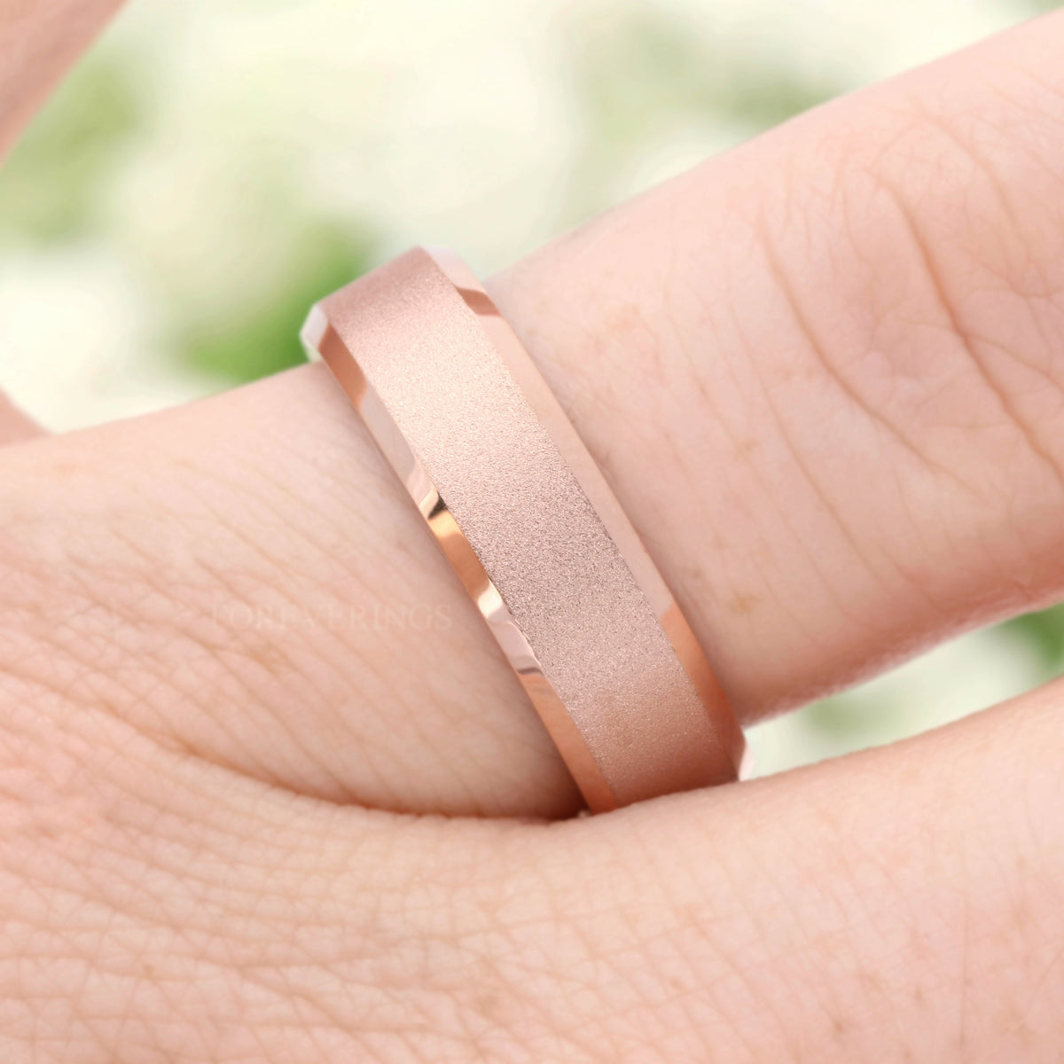 Sandblasted rose gold tungsten band on a finger, close-up of the beveled edge