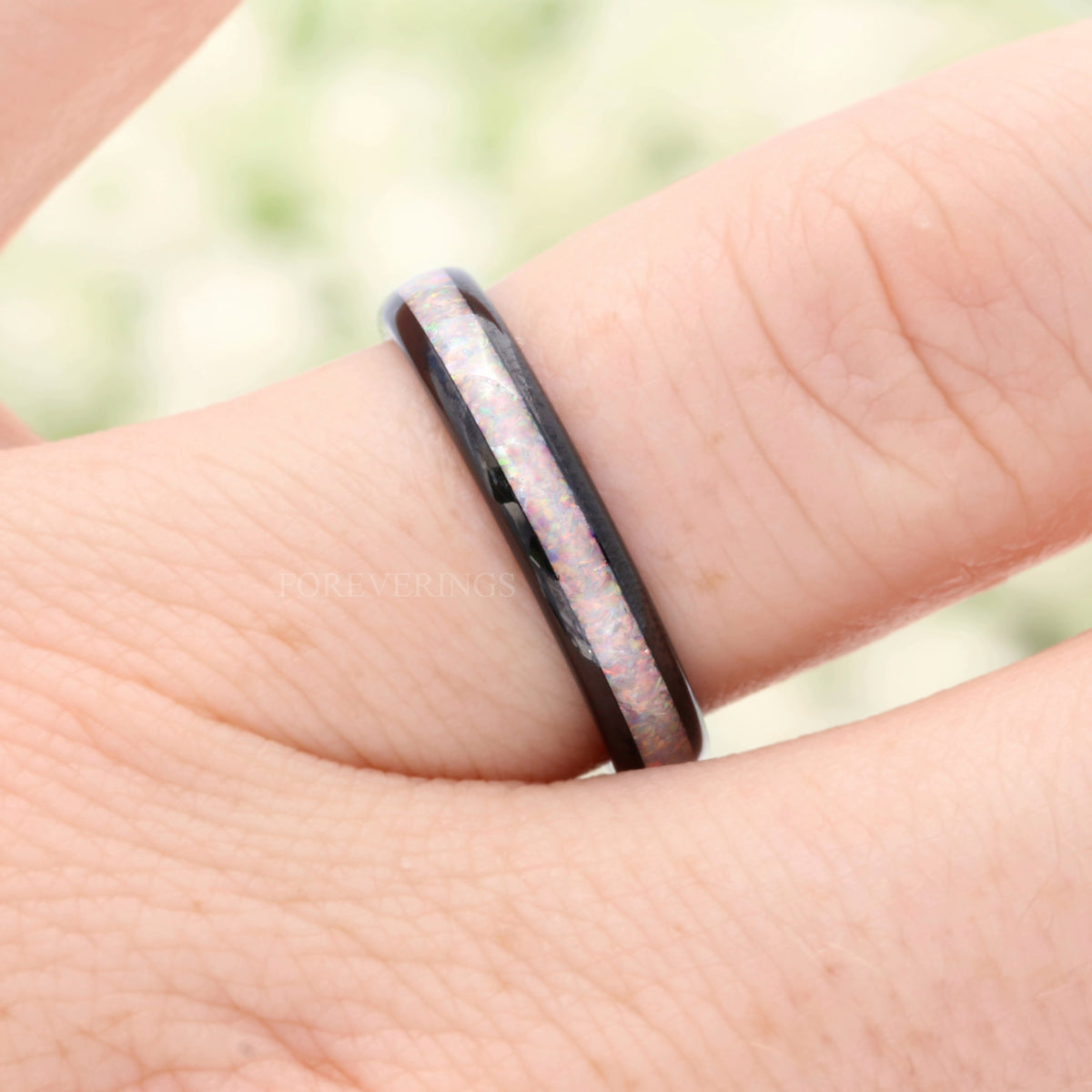 4mm black tungsten ring with white fire opal inlay on a finger, close view