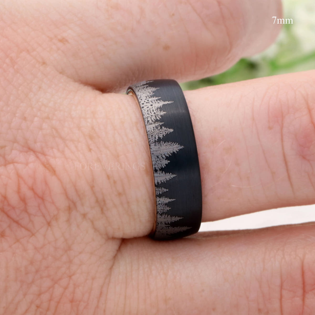 7mm black forest band with pine tree pattern worn on a finger