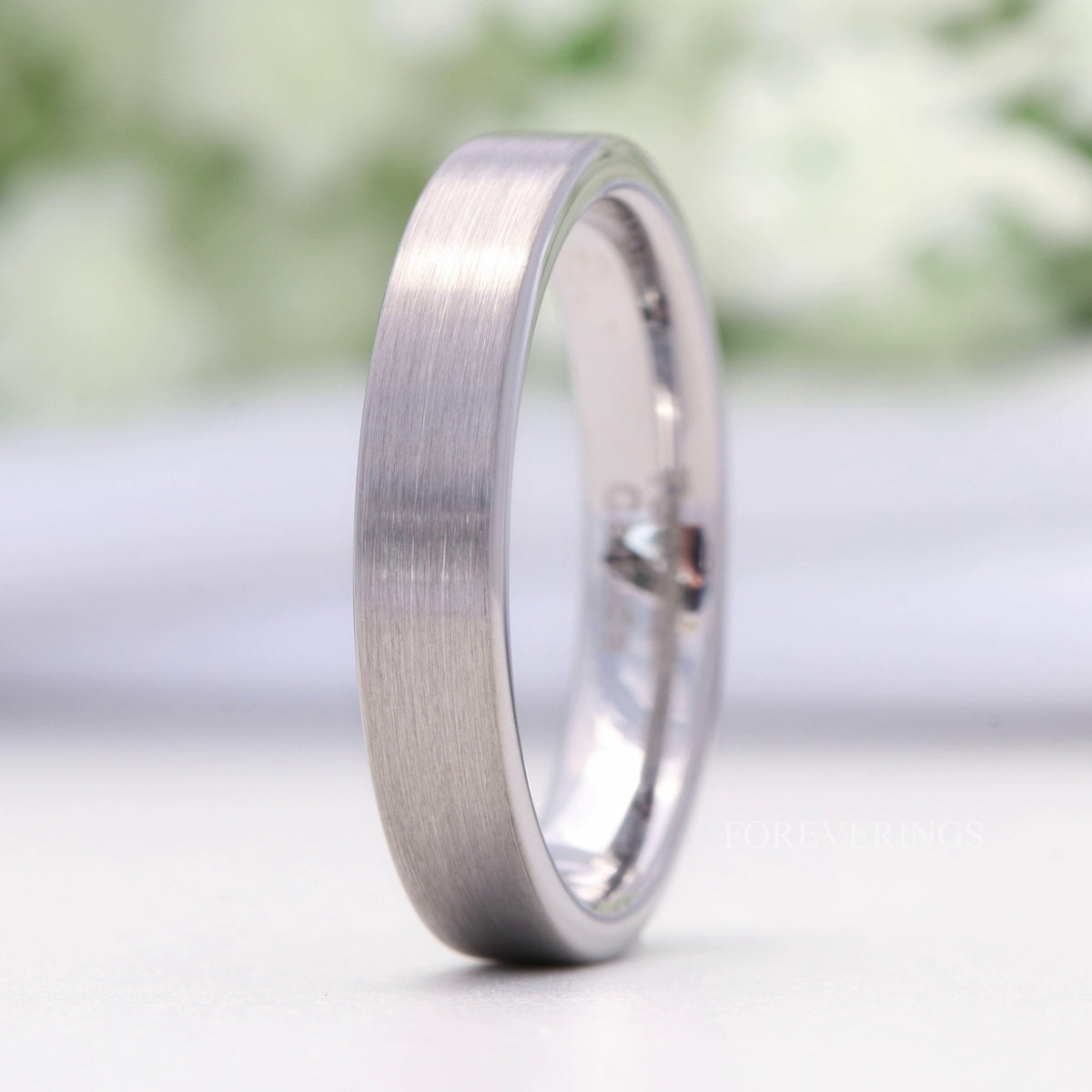 Minimalist 4mm silver tungsten band standing upright, the brushed outer surface facing forward