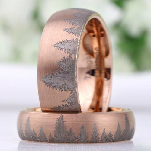 Men's rose gold tungsten bands with an etched pine forest pattern, one standing on the other