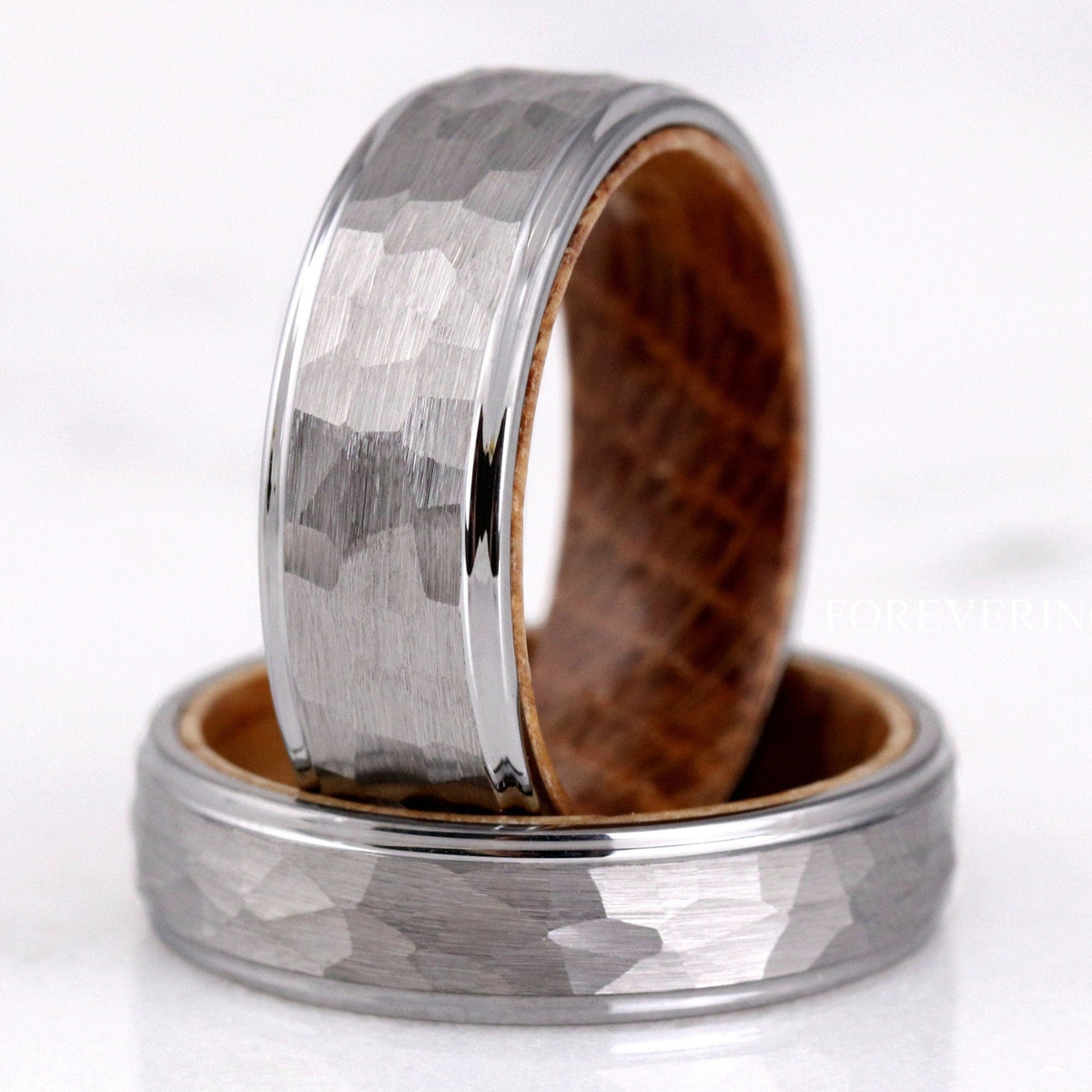 Two hammered silver tungsten bands with whiskey barrel wood lining, one standing on the other