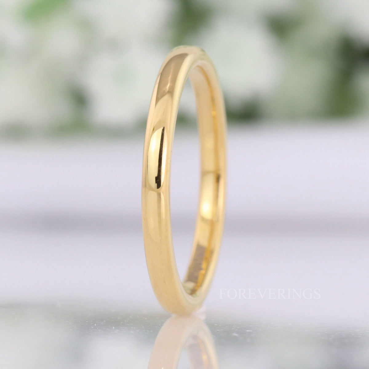 Thin 2mm gold tungsten wedding band standing upright, polished dome catching the light