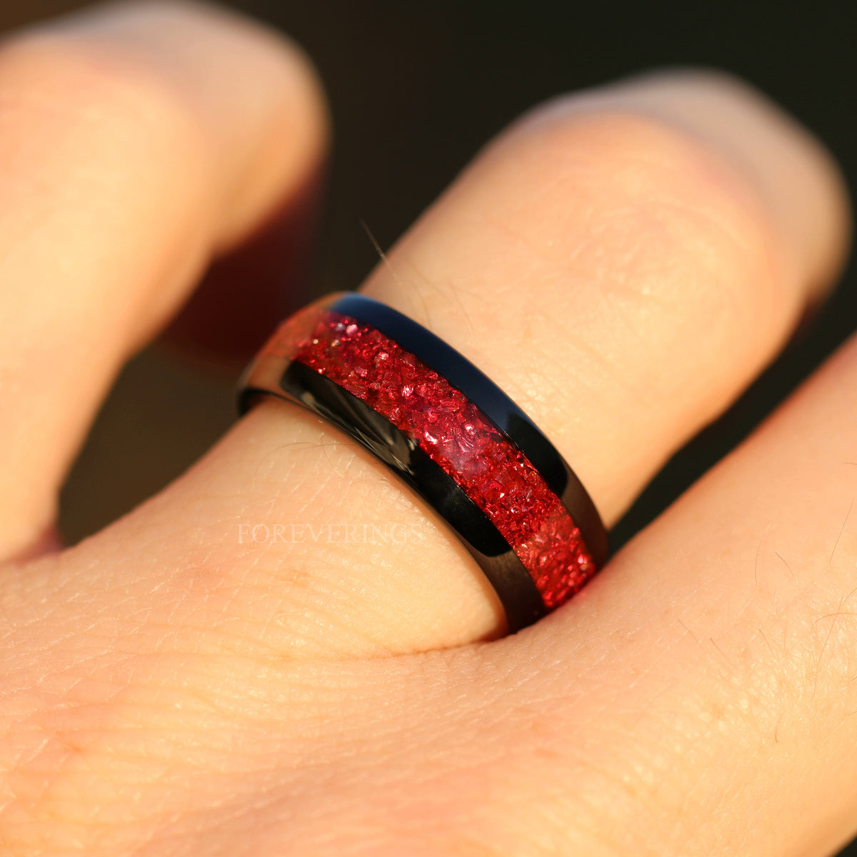 Men's 8mm black tungsten band with ruby inlay worn on a finger, close view