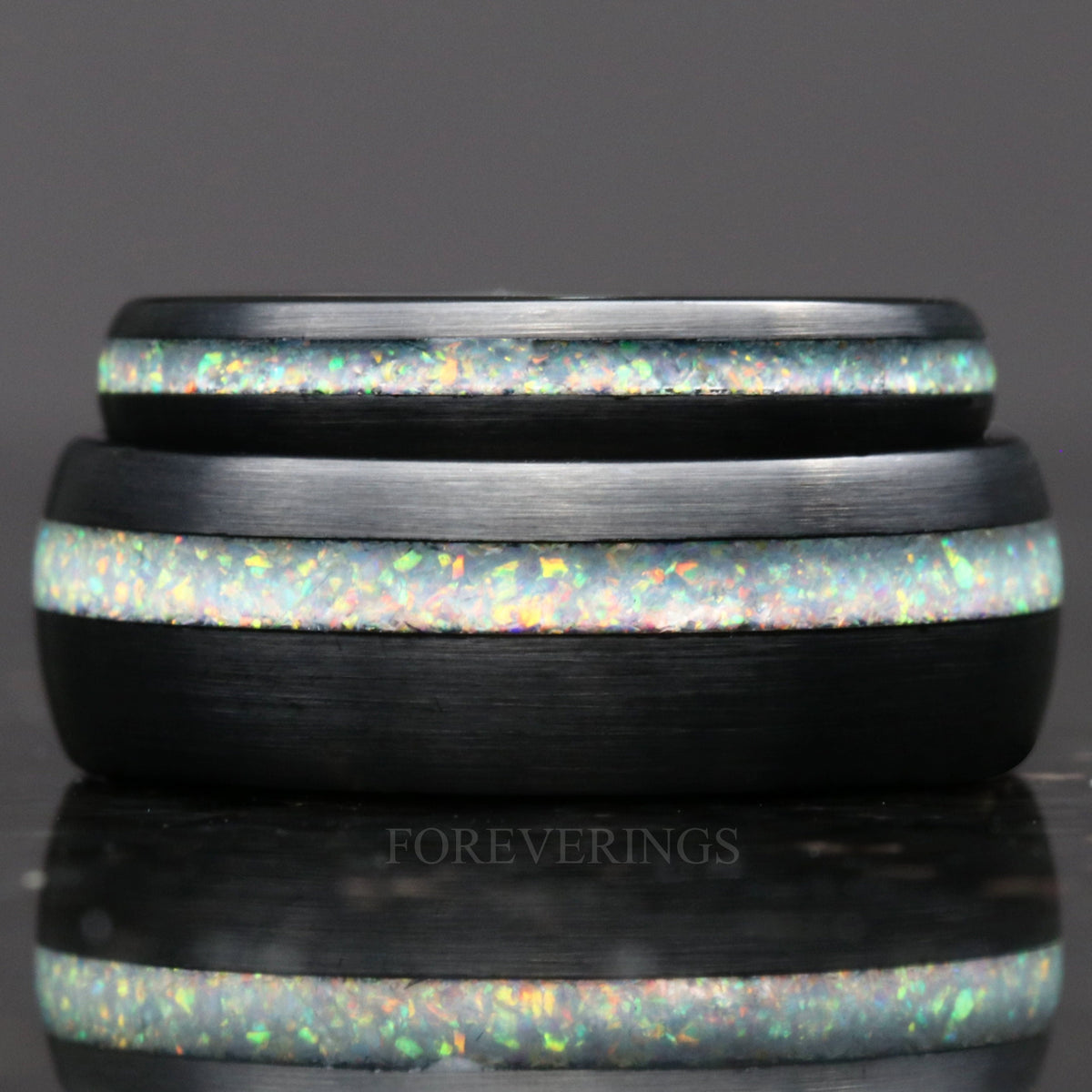 His and hers wedding bands in black tungsten with white fire opal, stacked and seen straight on
