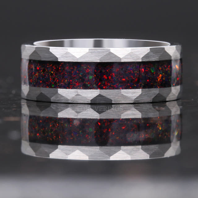 Hammered silver tungsten band with black fire opal inlay lying flat, faceted edges straight on