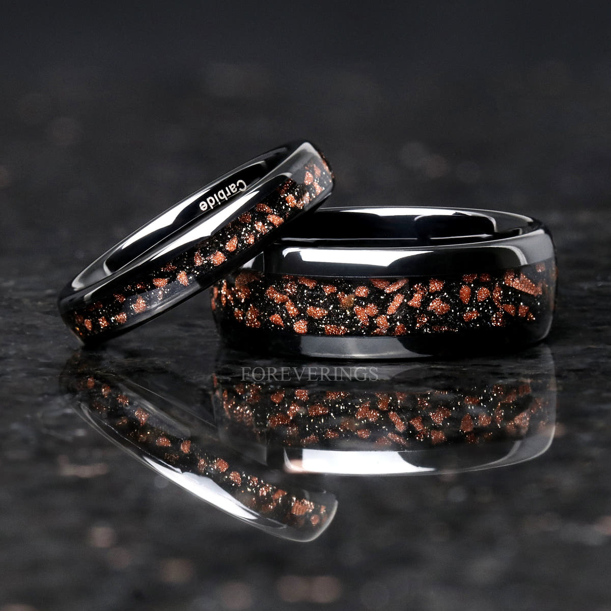 Thin red goldstone tungsten band leaning on a wider black band, reflection below