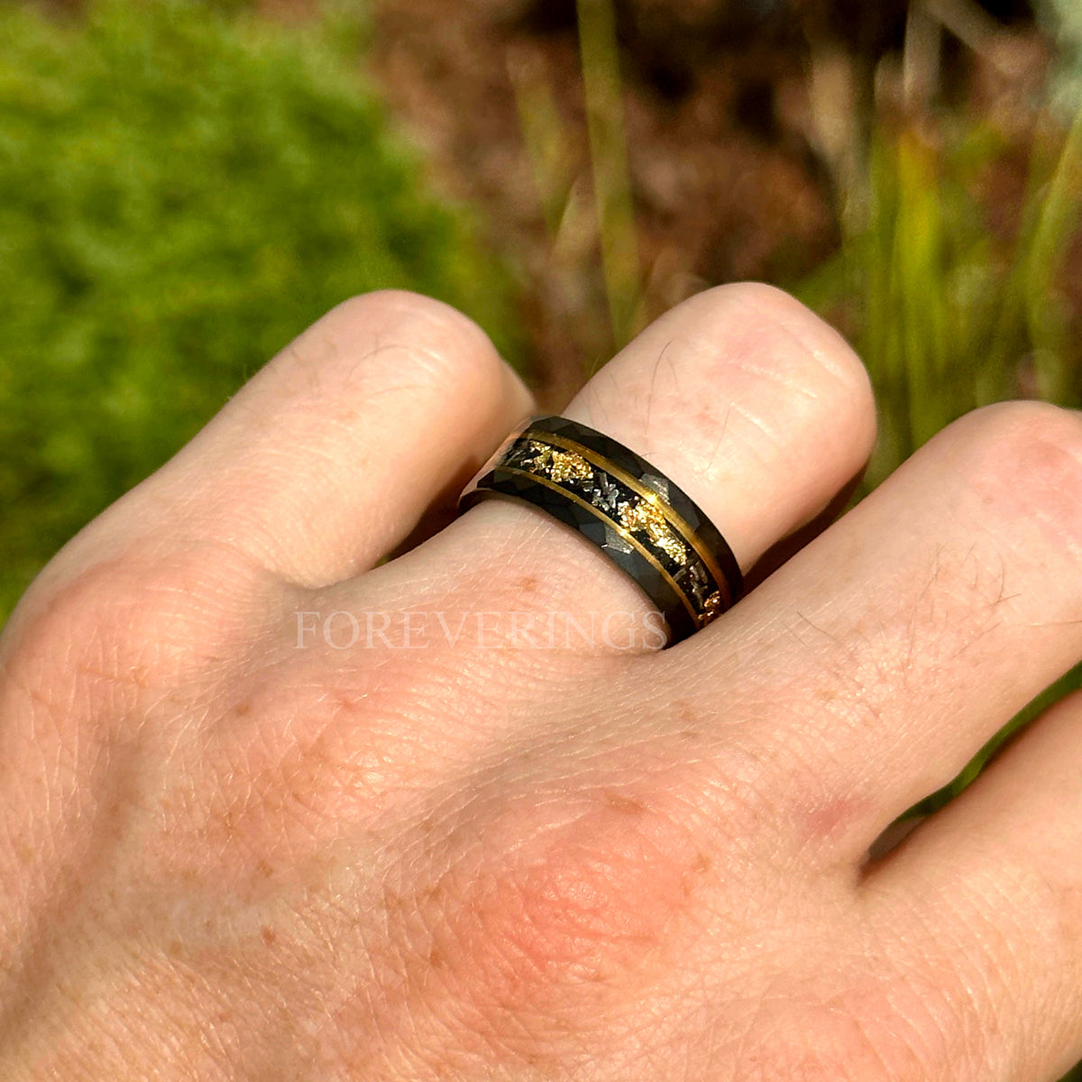 Two-tone black and gold meteorite wedding band worn on a man's hand