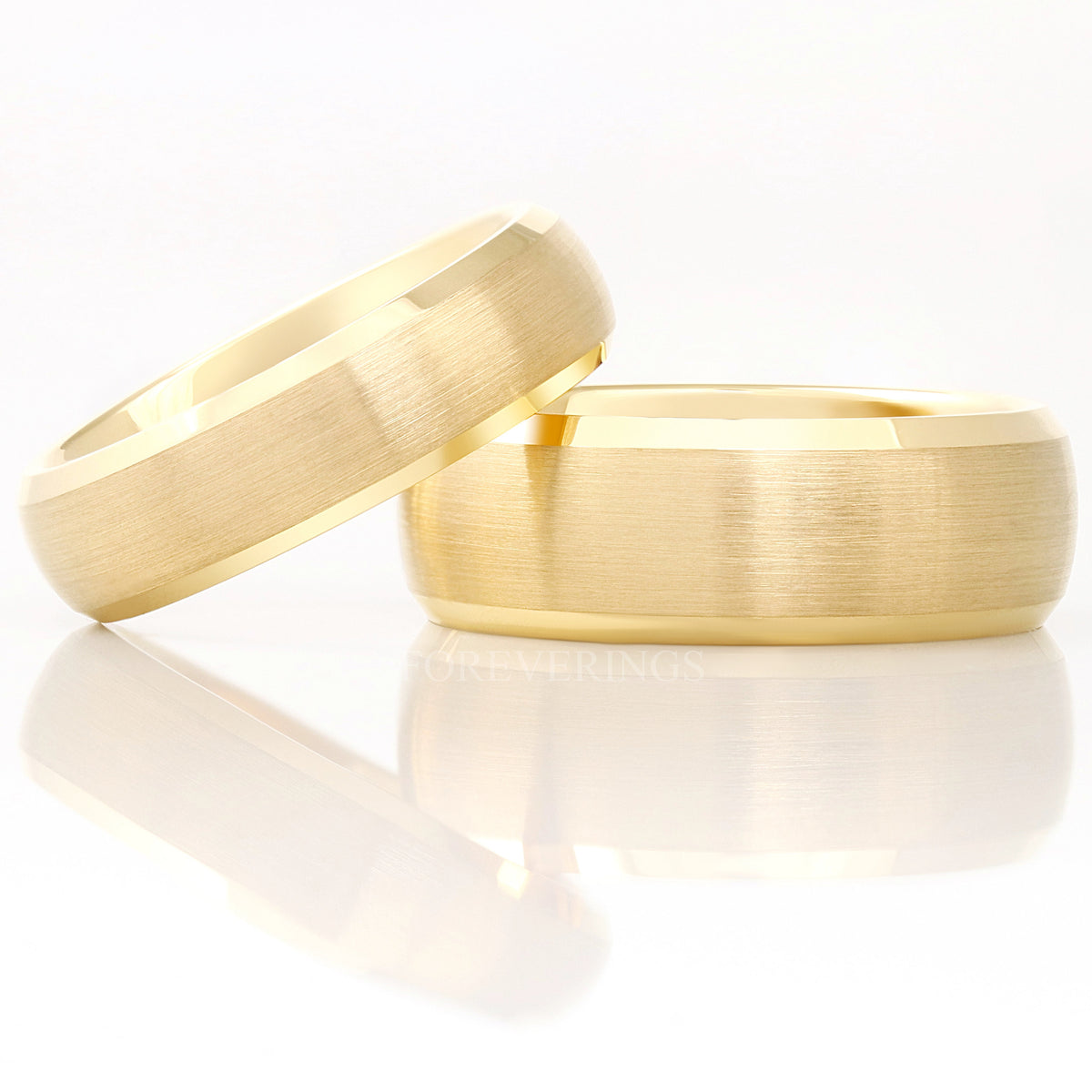 Brushed gold tungsten band leaning on a wider brushed gold band, both with beveled edges
