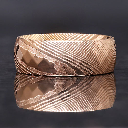Men's 8mm rose gold Damascus steel ring with hammered facets, lying flat with reflection below