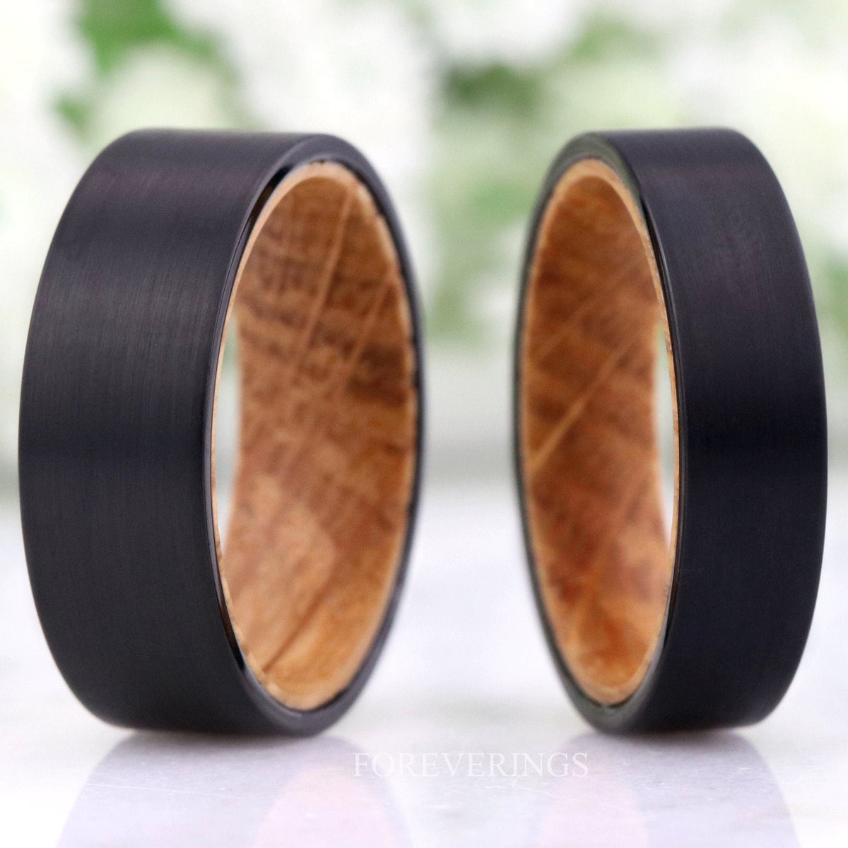 Men's black brushed tungsten wedding bands lined with whiskey barrel wood, standing side by side
