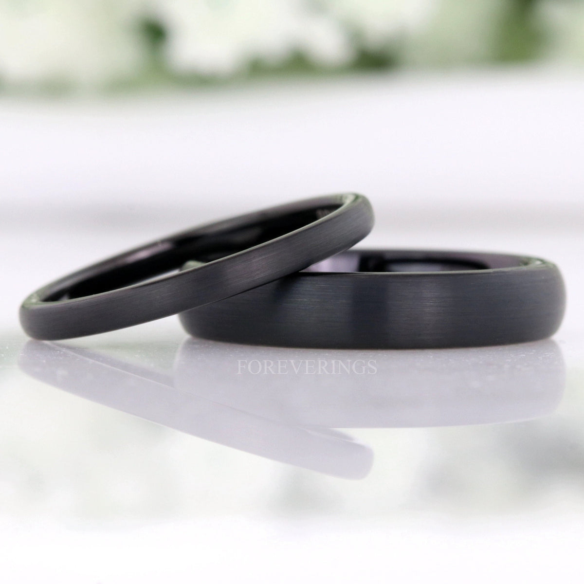 2mm and 4mm matte black tungsten wedding bands, the thin band leaning on the wider one