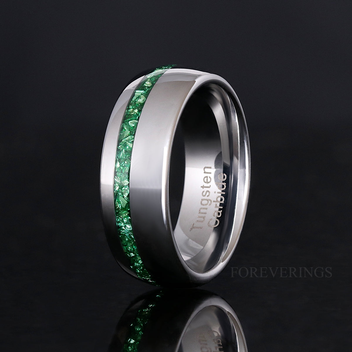Polished silver tungsten ring with emerald inlay standing on edge, wider view