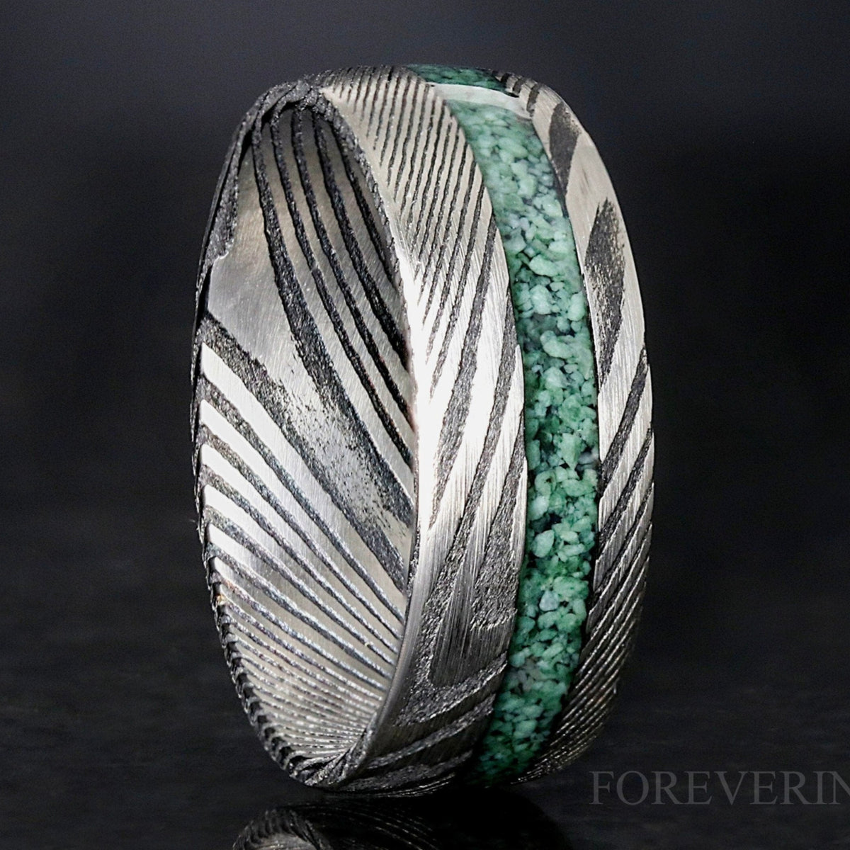 Men's 8mm Damascus steel ring with crushed green moss agate inlay, standing on edge