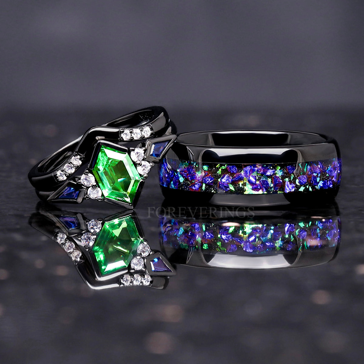Black tungsten ghost nebula band beside a black engagement ring with a green center stone