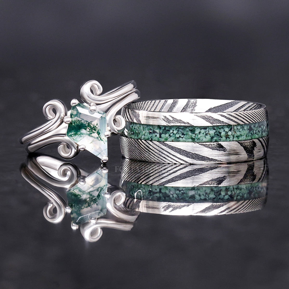 Silver moss agate twirl ring beside a wide Damascus steel band with moss agate inlay