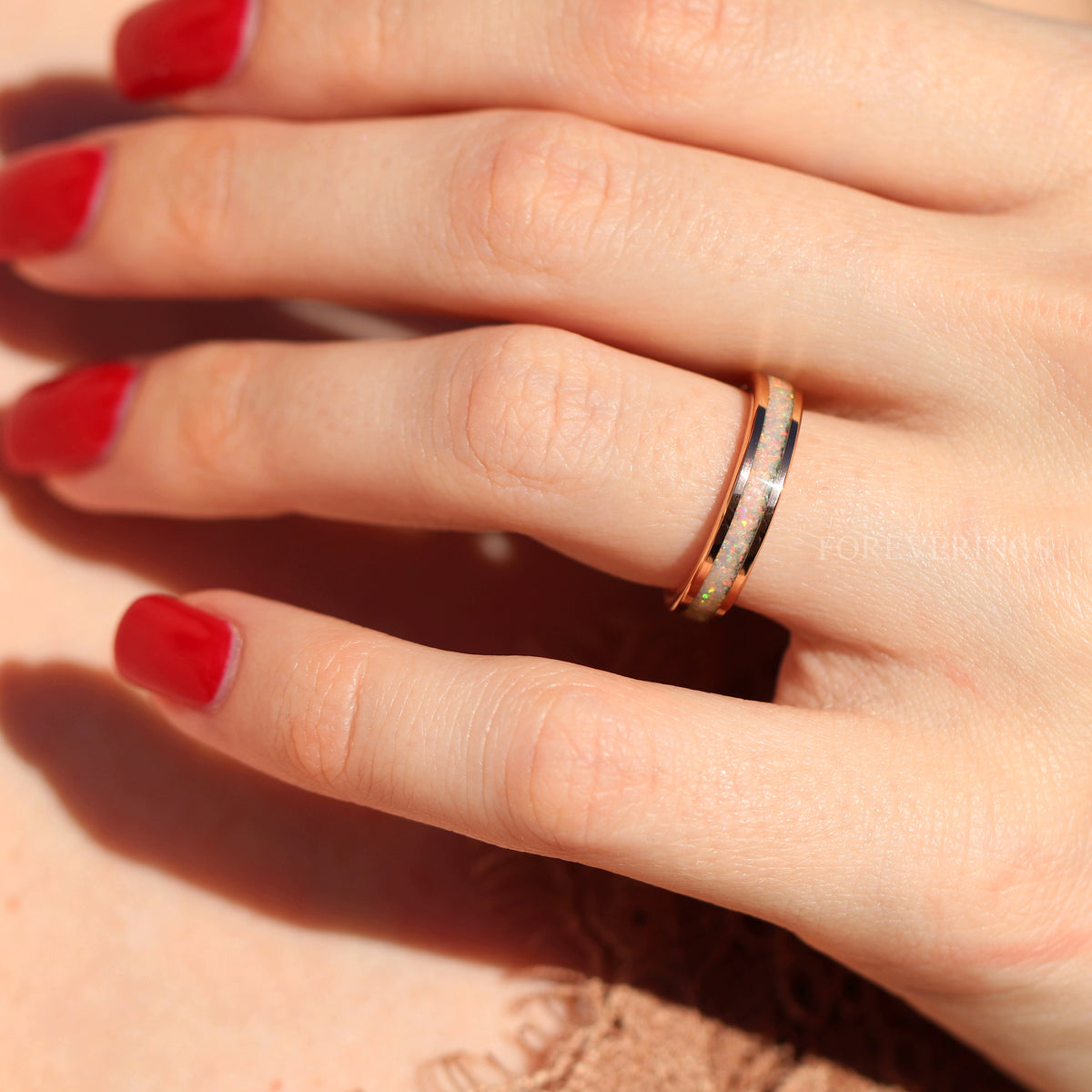 Women's 4mm rose gold tungsten ring with white fire opal inlay worn on a hand