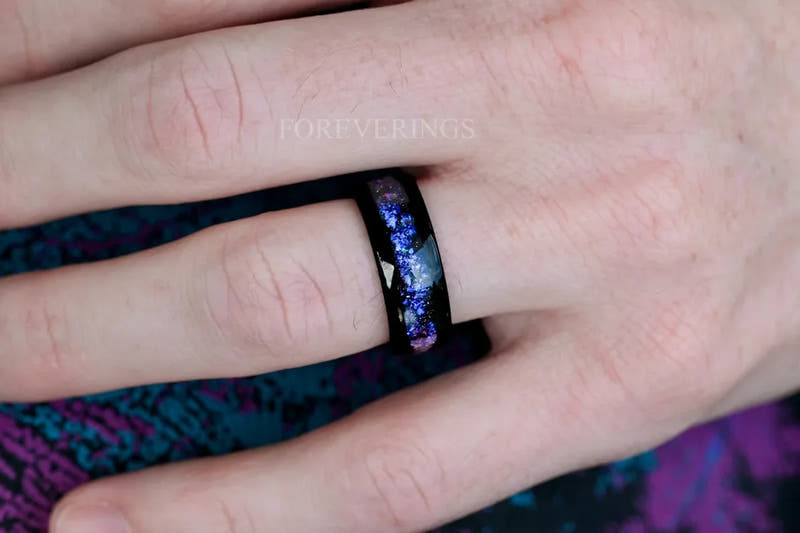 Men's black tungsten wedding band with blue nebula opal inlay worn on his hand