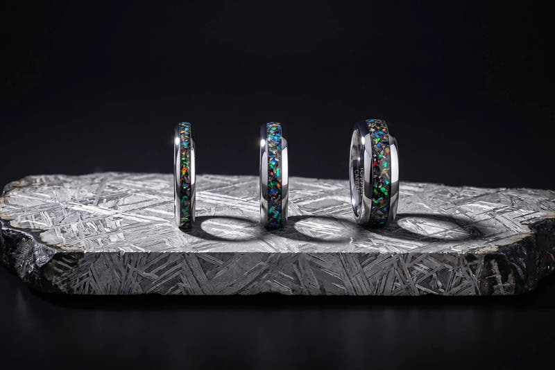Three meteorite rings with opal inlays standing on an etched meteorite slab