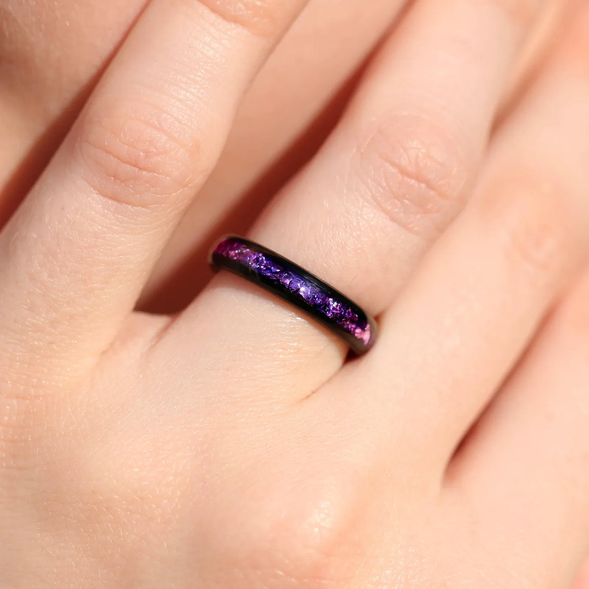 Women's black tungsten wedding band with amethyst inlay worn on her hand