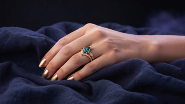 Engagement ring worn on the ring finger of a left hand on a dark surface