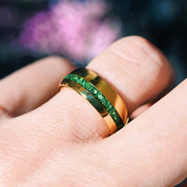 Gold tungsten band with an emerald stripe worn on a man's hand, close crop