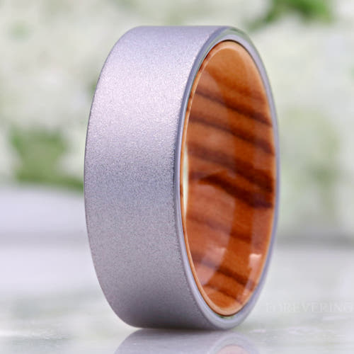 Men's 8mm sandblasted silver tungsten wedding band with an olive wood interior, standing on edge