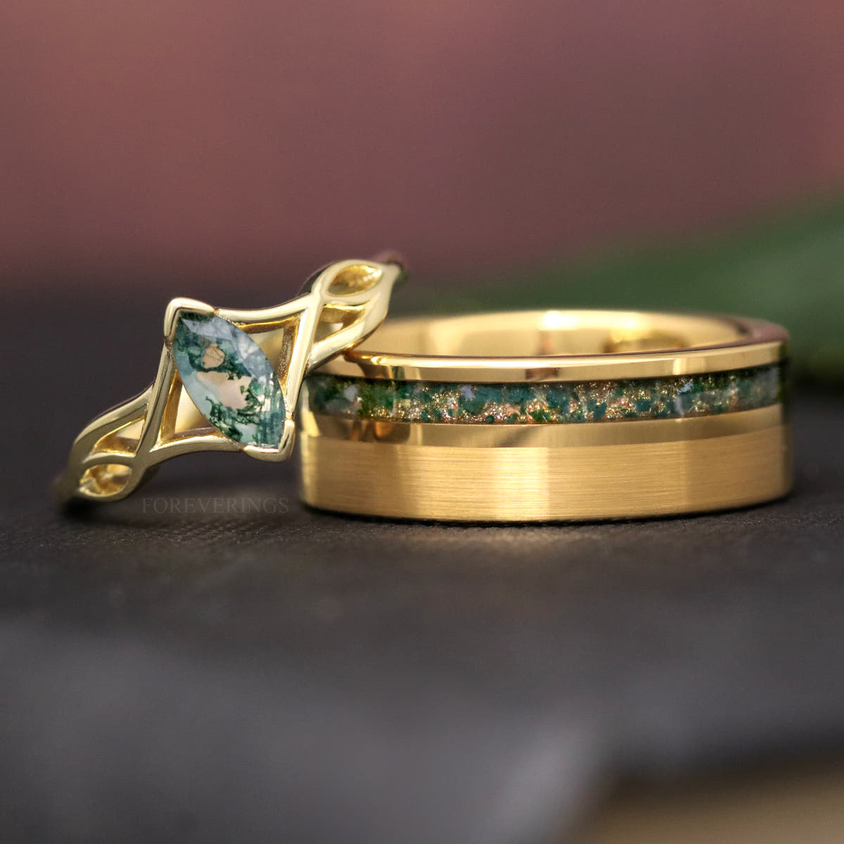 Gold moss agate engagement ring beside a wider brushed gold band with moss agate inlay