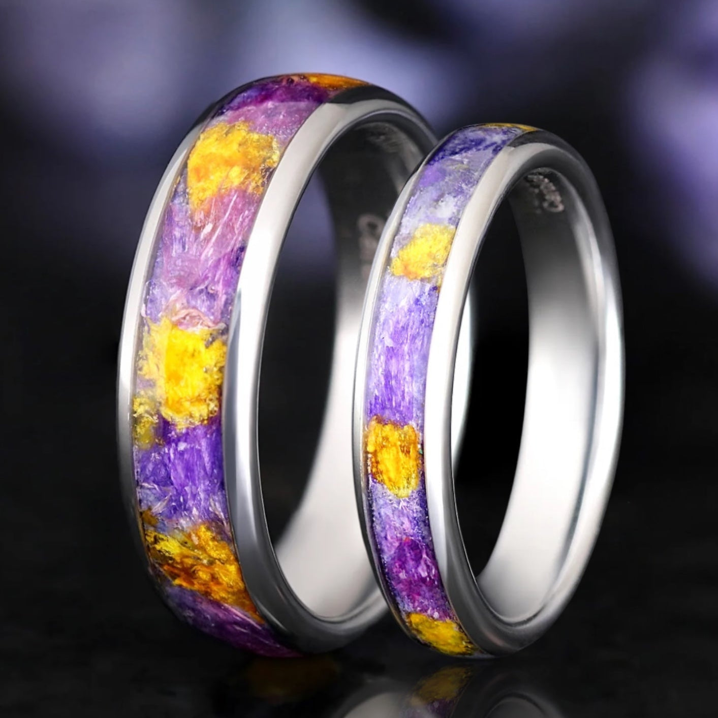 Two rings with forget me not flower that's purple and yellow inlay on a dark background