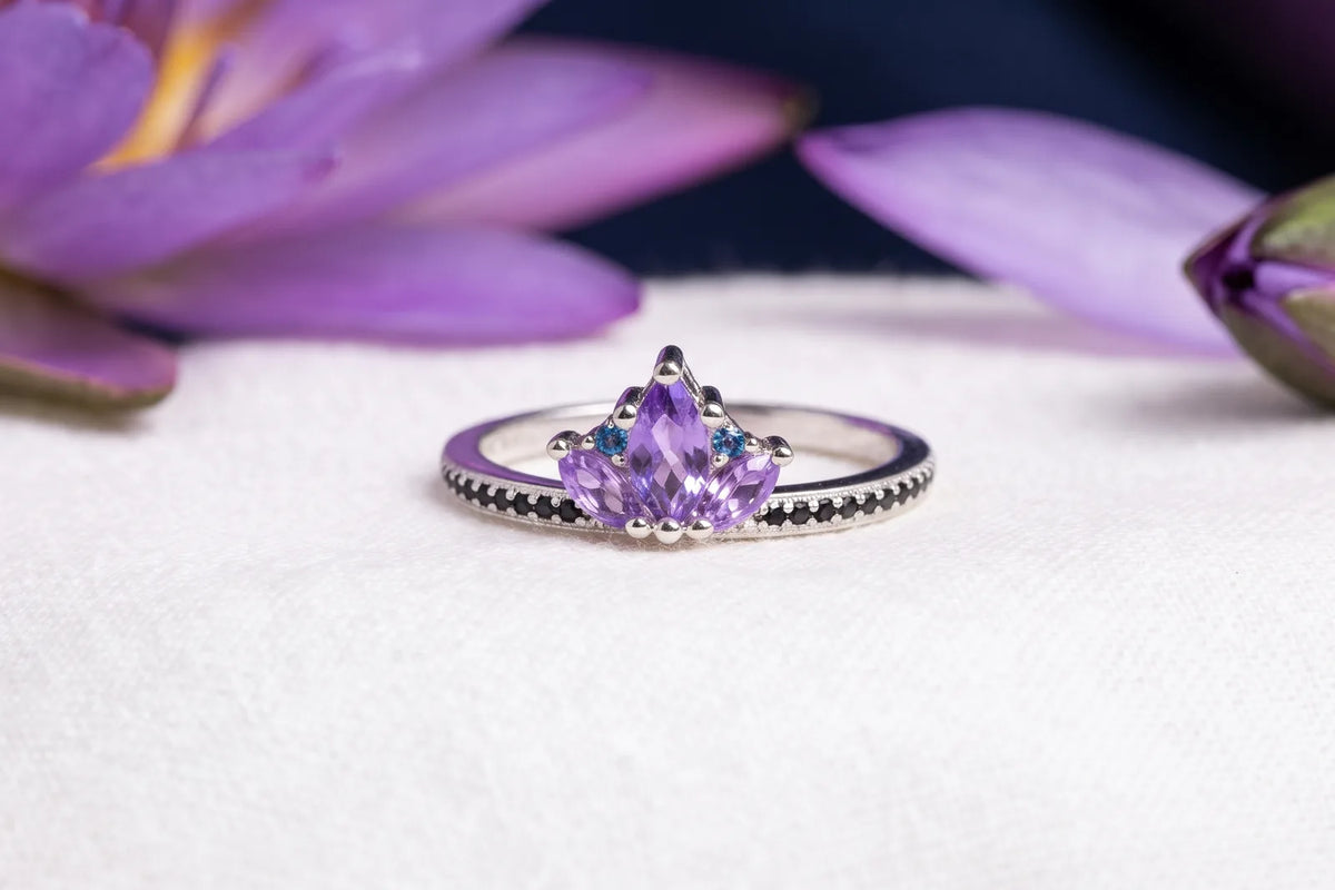 Amethyst lotus ring with marquise petal stones on a silver band beside lotus flowers