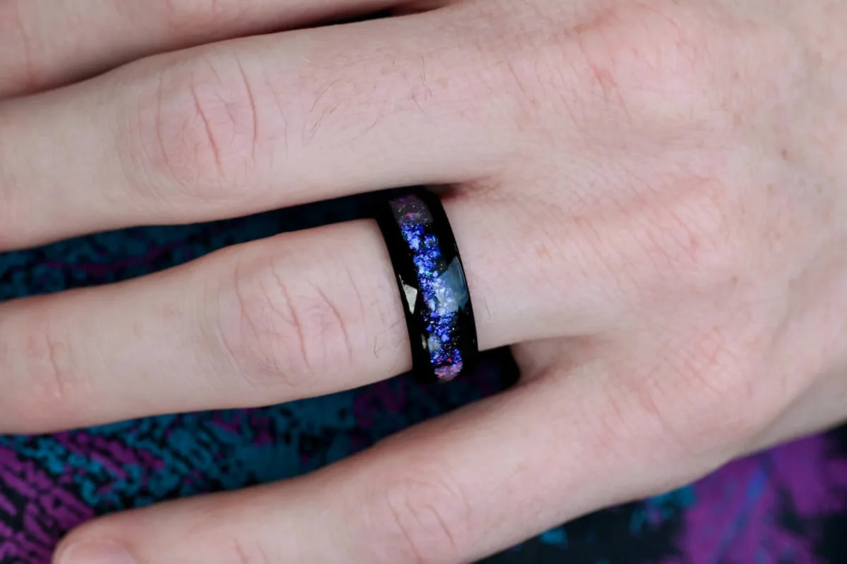 Mens black tungsten wedding band with blue nebula opal inlay worn on his hand