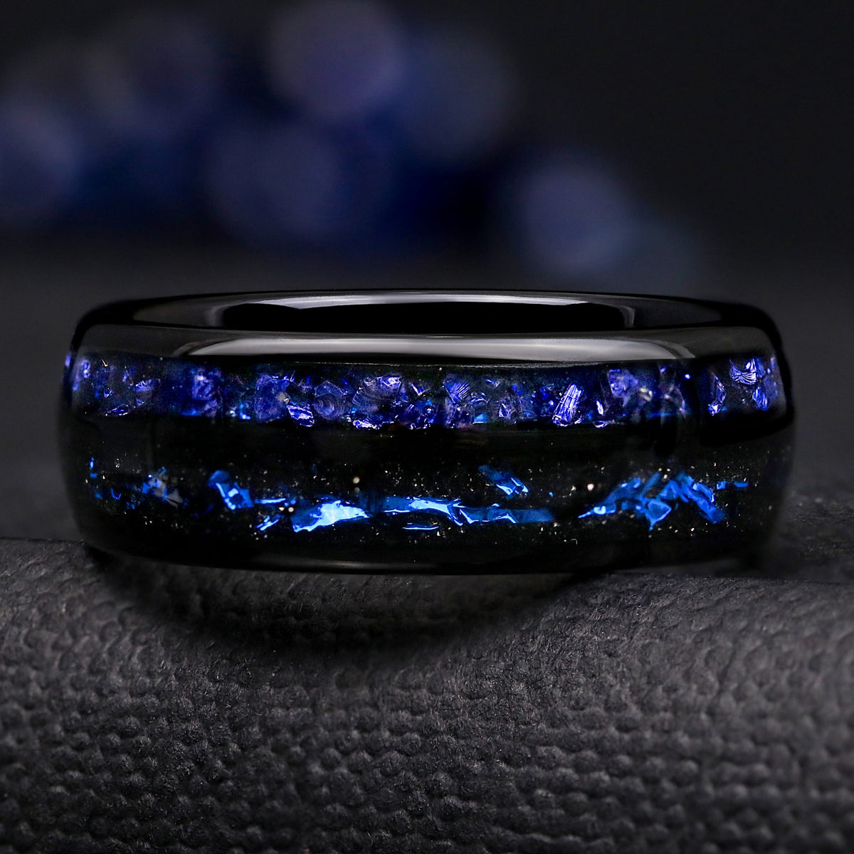 Men's 8mm black tungsten band shown straight on, crushed blue sapphire above black sandstone and blue foil