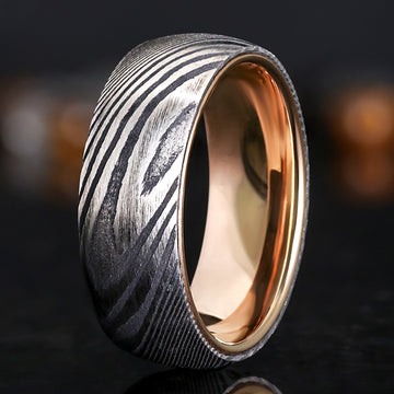 Angled view of an 8mm mens Damascus steel wedding band with a twisting black and silver pattern and a polished rose gold interior.