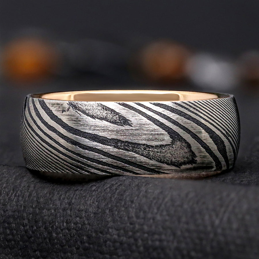 Side view of an 8mm Damascus steel wedding band showing the domed profile, black and silver grain, and rose gold interior at the rim.
