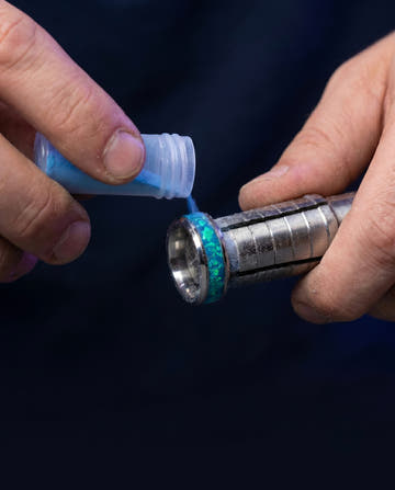 Jeweler hand-pouring crushed blue opal into the inlay channel of a tungsten ring
