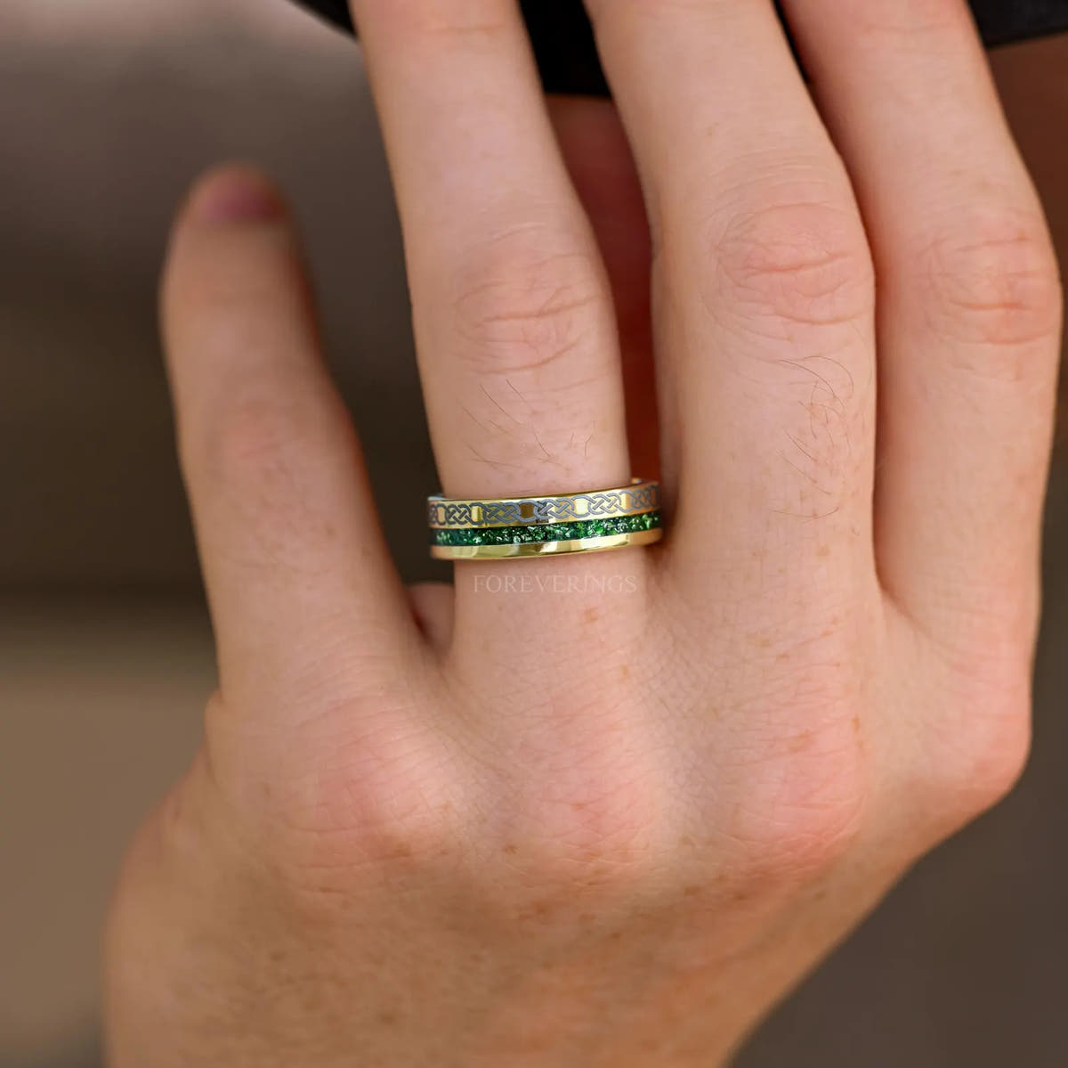 Gold tungsten wedding band with emerald inlay worn on a hand, knot pattern stripe facing out