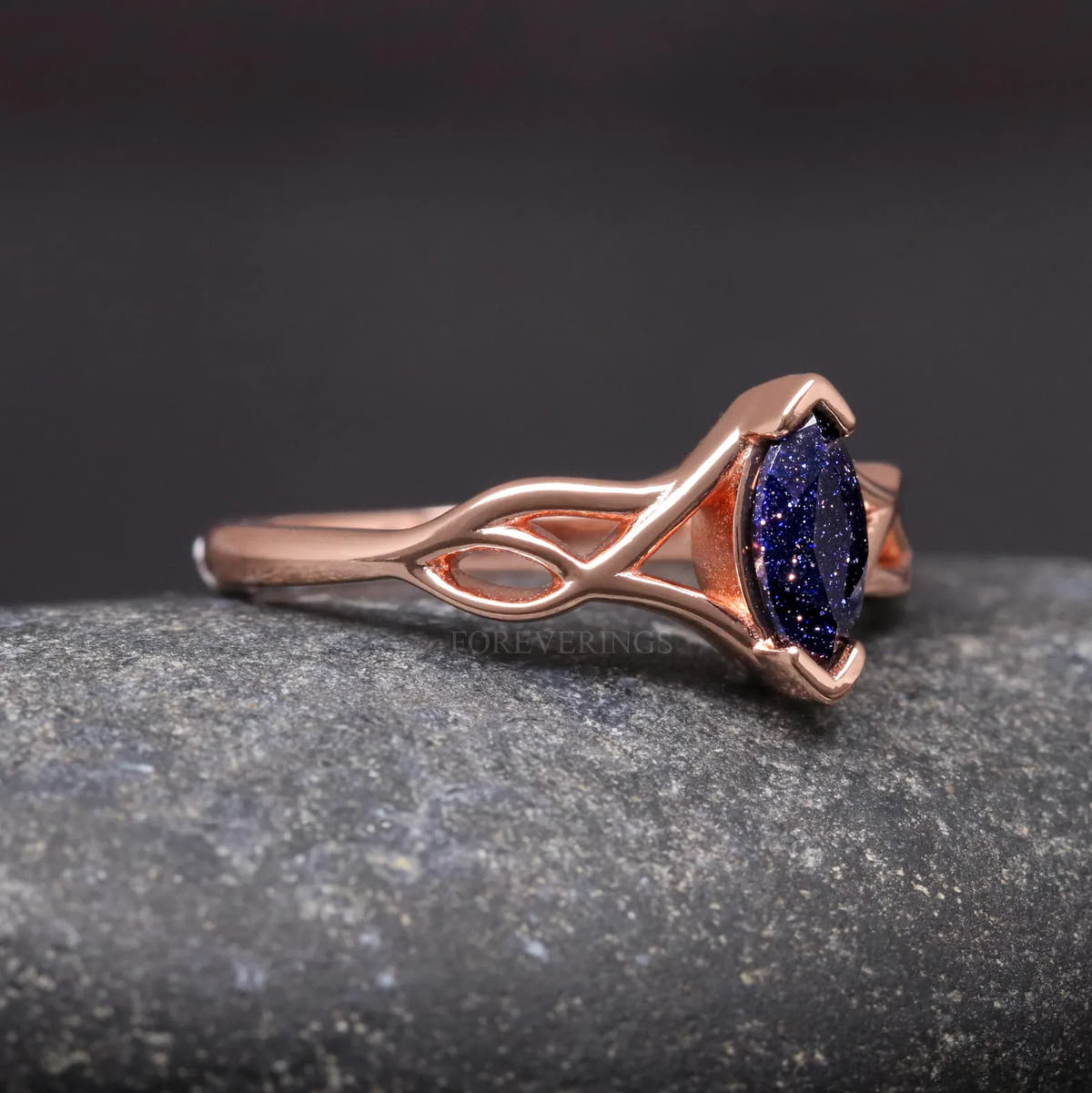 Rose gold Celtic knot ring from the side, woven shoulders leading to the marquise blue sandstone