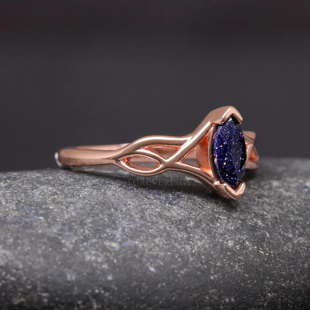 Rose gold Celtic knot ring from the side, woven shoulders leading to the marquise blue sandstone
