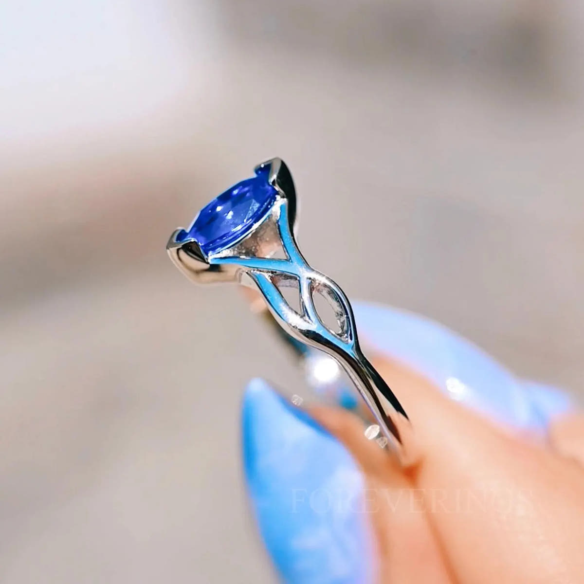 Sapphire Celtic knot ring held in fingertips, angled to show the open knot band
