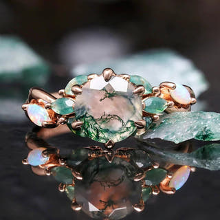 Women's rose gold sterling silver engagement ring with a moss agate center and white opal side stones