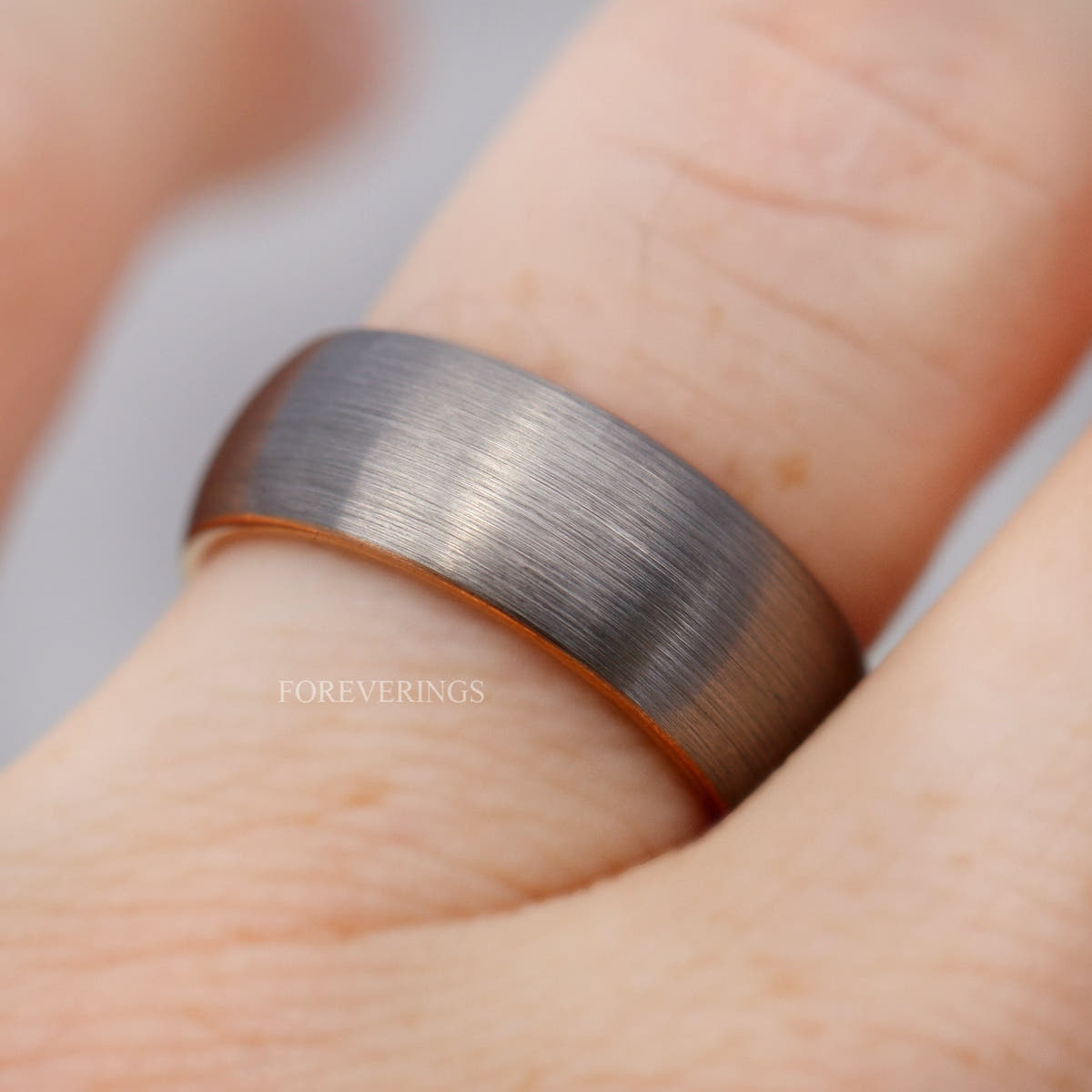 Men's 8mm matte silver tungsten band worn on a finger, rose gold edge showing
