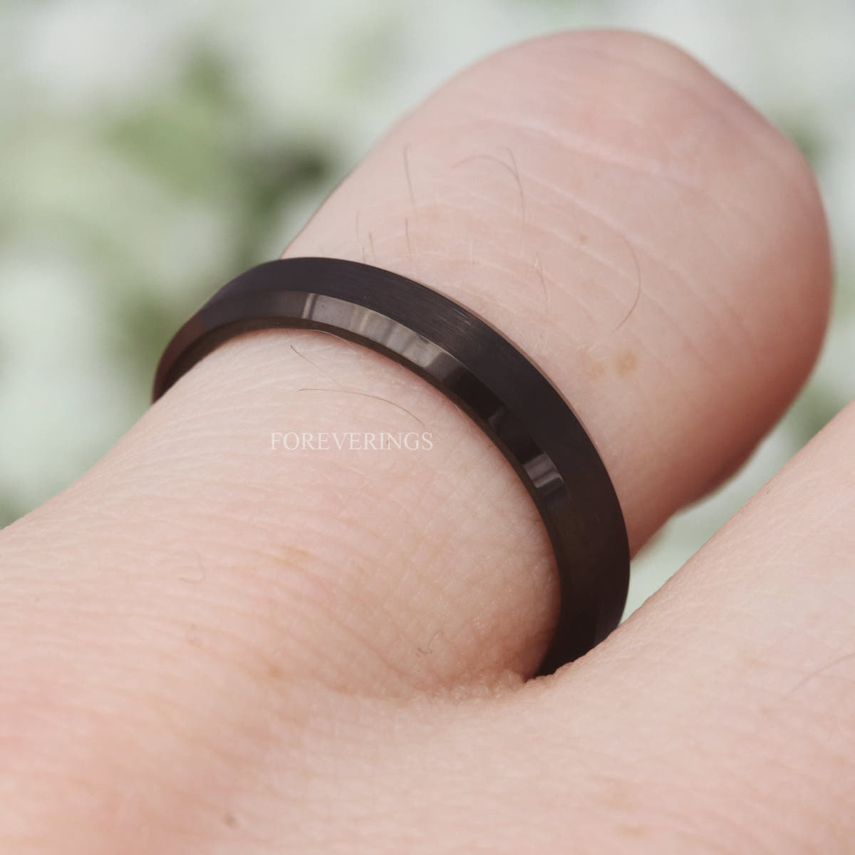 Matte black tungsten ring worn on a bent finger, angled close-up