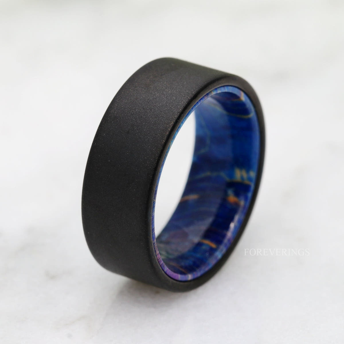 Sandblasted black tungsten and blue elder wood band standing at an angle on white marble