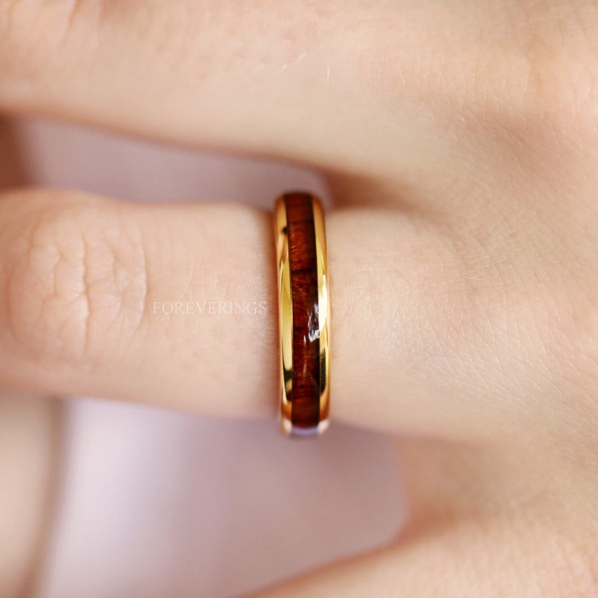 Gold tungsten koa wood band worn on a finger, side view