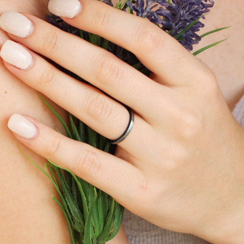 Thin brushed silver and blue tungsten wedding band worn on a hand, wider view