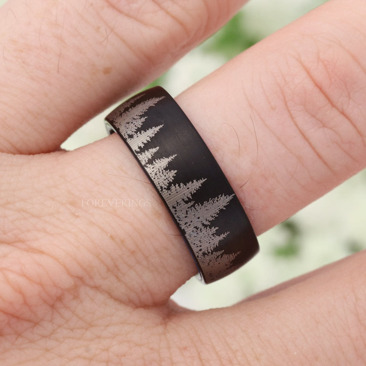 Black tungsten forest band with blue wood lining worn on a finger, straight on