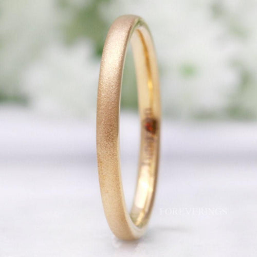 Minimalist women's 2mm gold sandblasted tungsten wedding band, standing on edge in a close crop