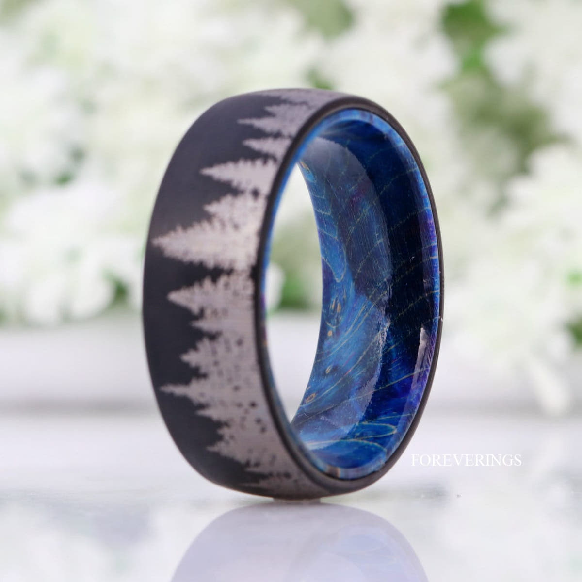 Black tungsten tree line wedding band standing upright, blue wood interior visible