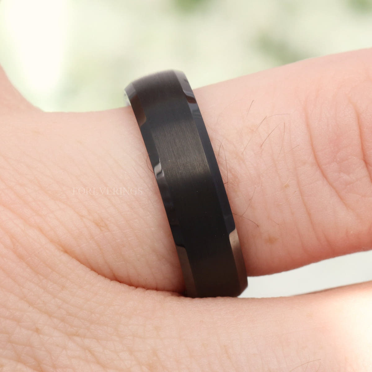 Black tungsten beveled band on a hand, angled side view