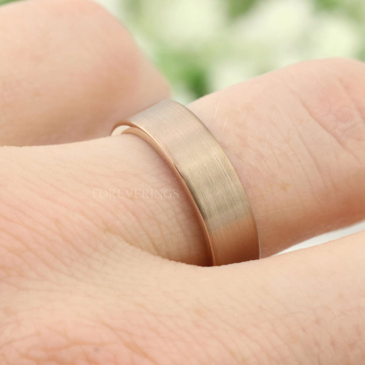 Rose gold tungsten band worn on a finger, low-angle close-up